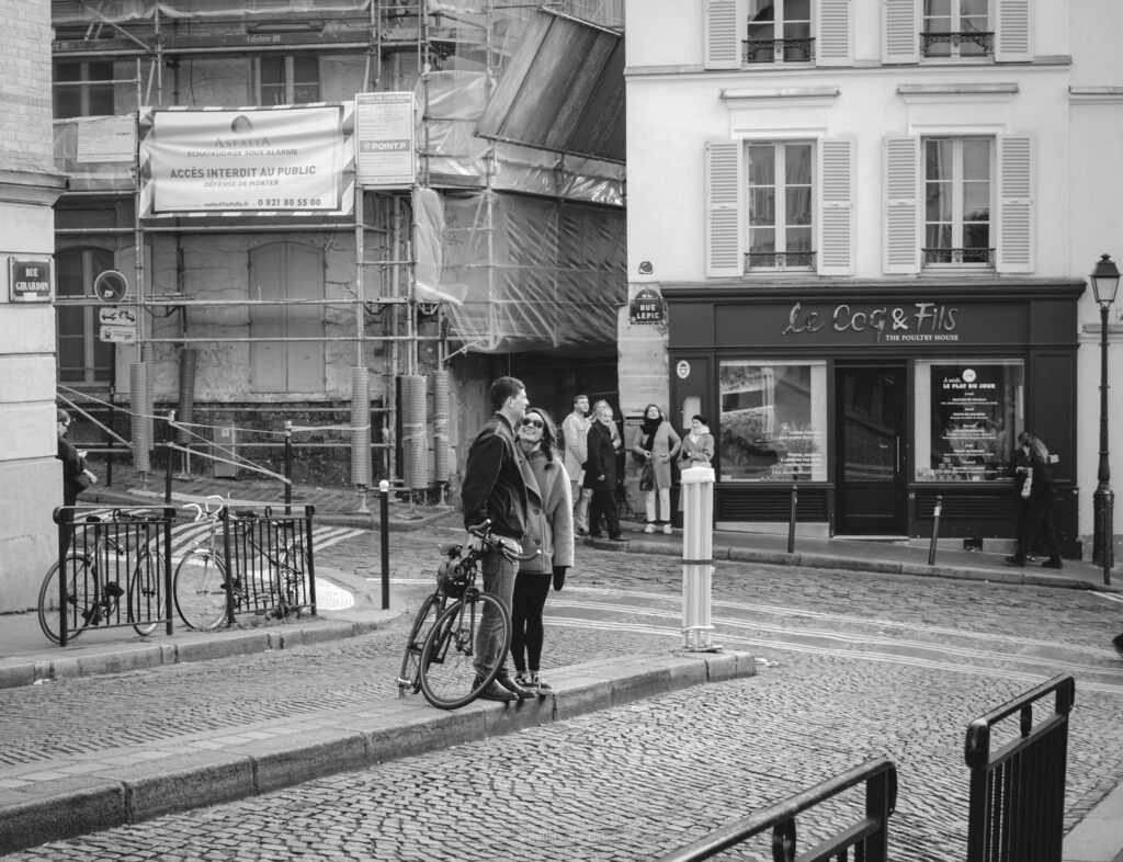 Scène de rue à Montmartre : couple rue Lepic et Girardon Couple souriant avec un vélo au coin de la Rue Lepic et Rue Girardon à Paris devant le restaurant Le Coq & Fils.