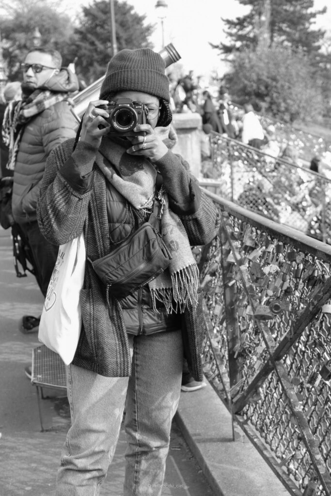 Photographe au Pont des Arts : Portrait Noir et Blanc Photographe avec appareil Fujifilm devant les cadenas d'amour d'un pont à Paris, style noir et blanc.